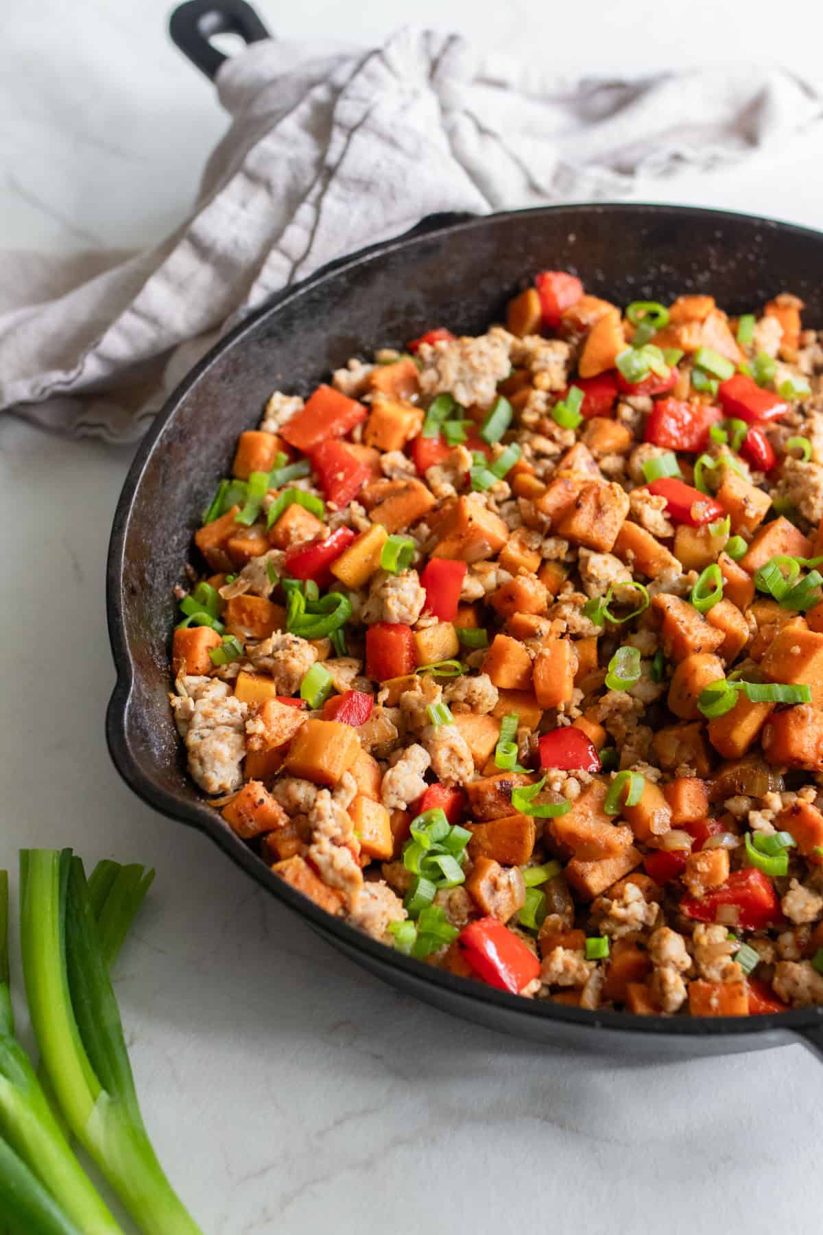 Sweet potato hash topped with green onions in a cast iron skillet.
