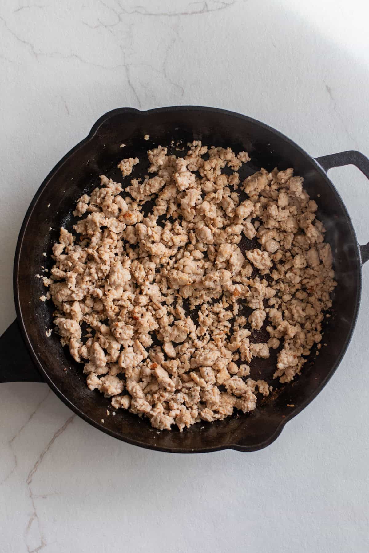 Cooked crumbled sausage in a cast iron skillet.