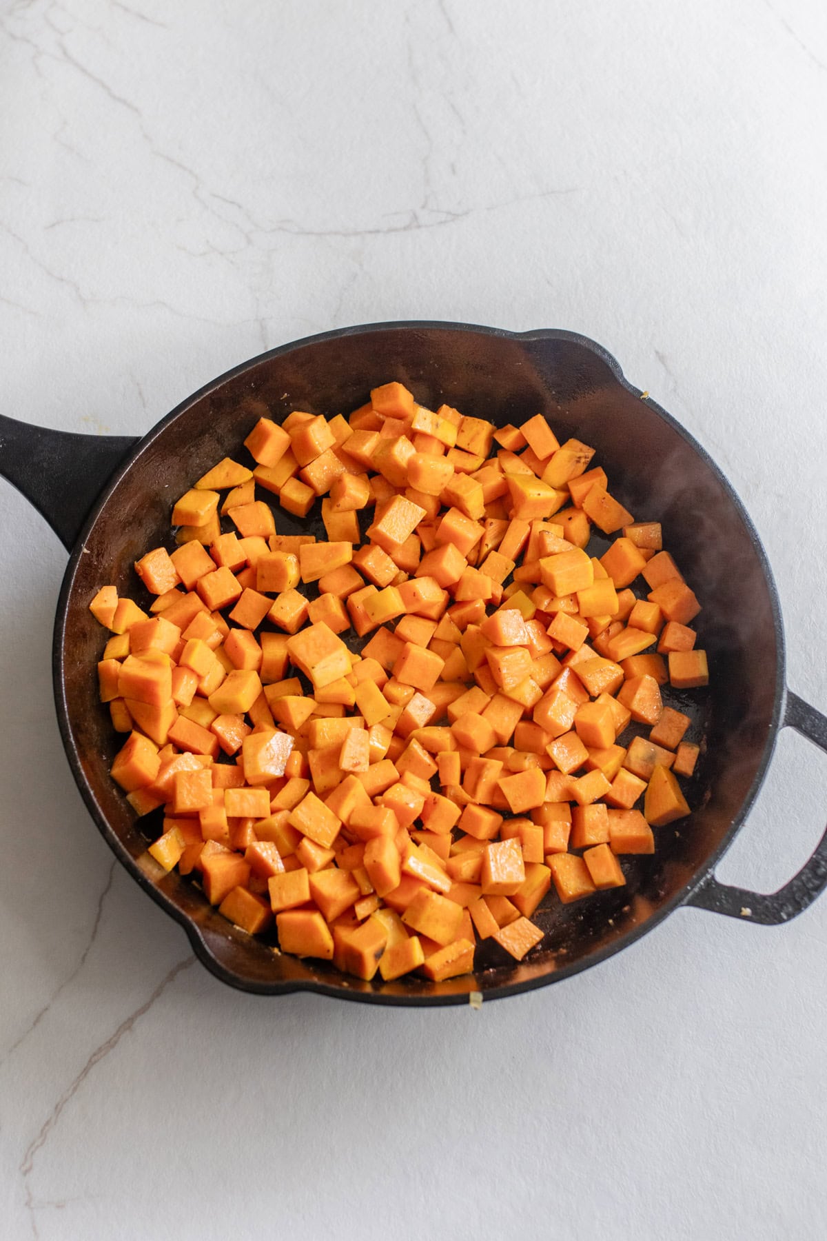Cubed sweet potatoes browning in a cast iron skillet with olive oil.