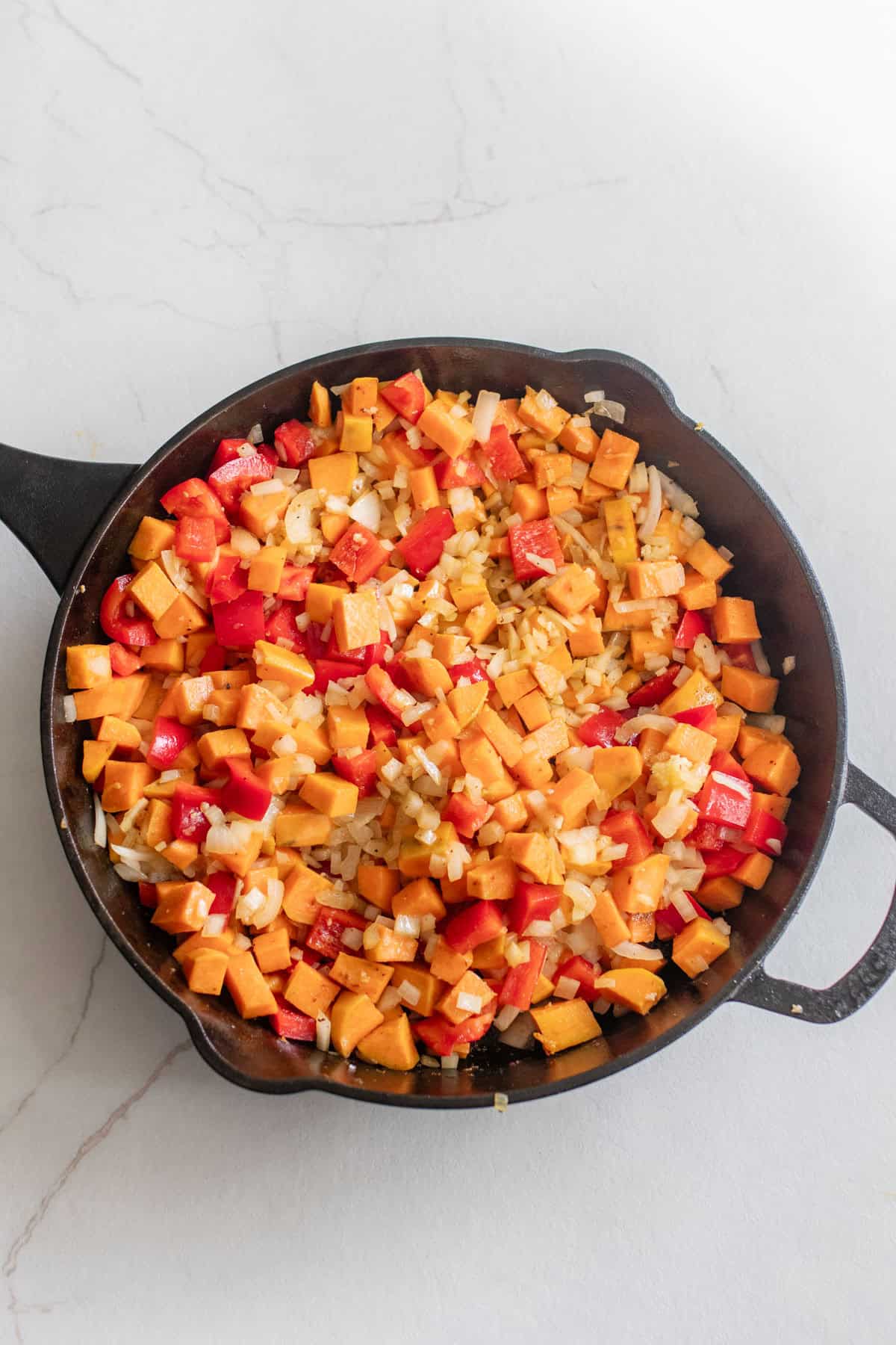 Onion, bell pepper, and sweet potato cooking in a cast iron skillet.