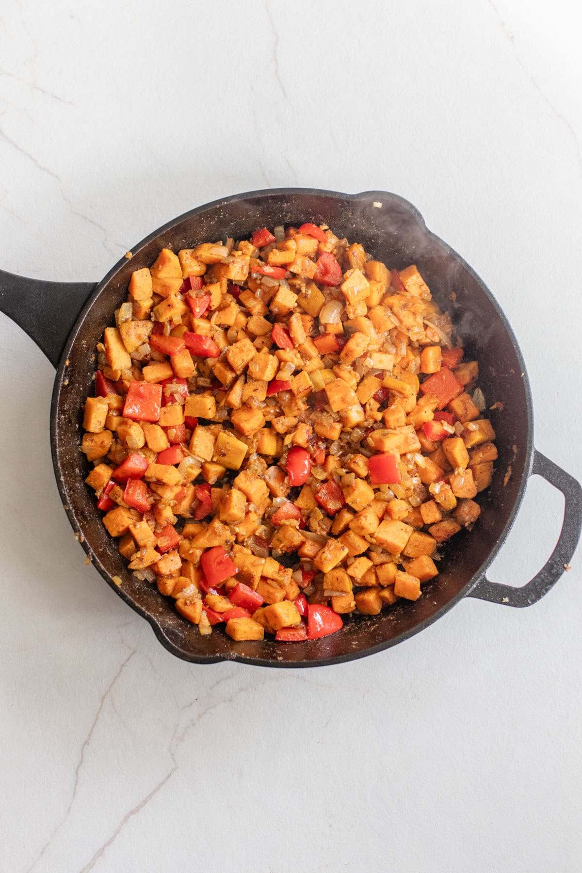 Sweet potato, onion, bell pepper, and seasonings cooking in a cast iron skillet.