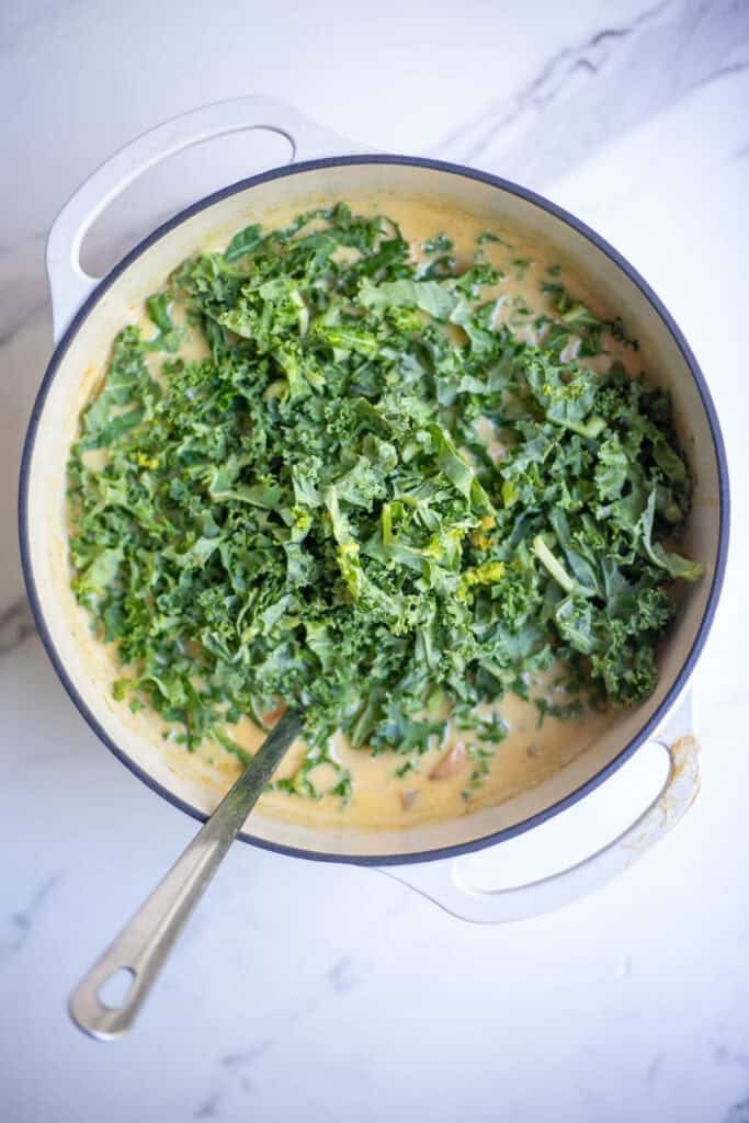 Kale added to a Dutch oven full of soup.