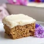 a square piece of cake that is frosted with white cream cheese frosting.