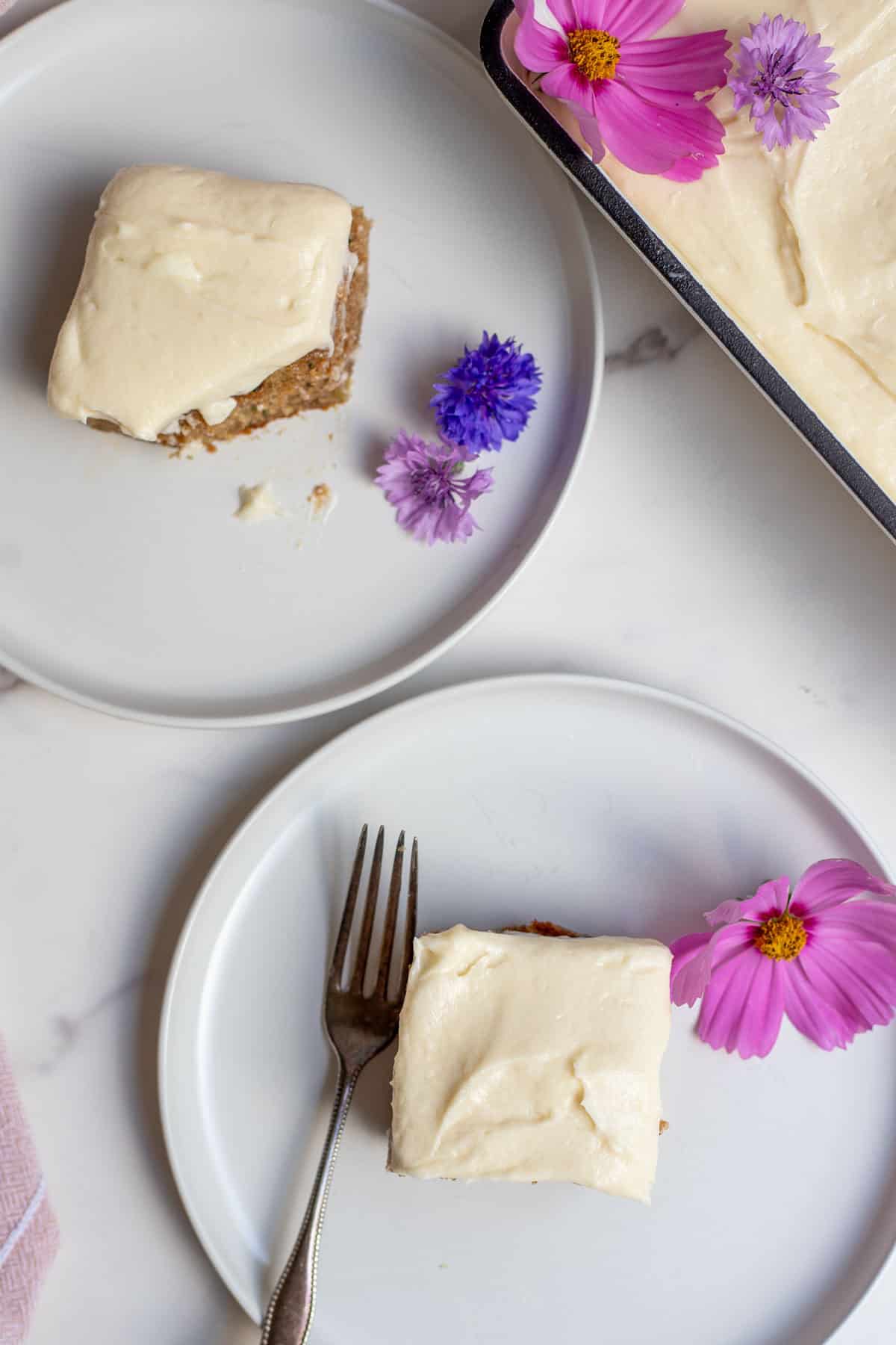 Two pieces of frosted cake on two small white plates.