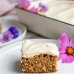 a slice of frosted cake sitting on a white plate with a pink flour beside it.