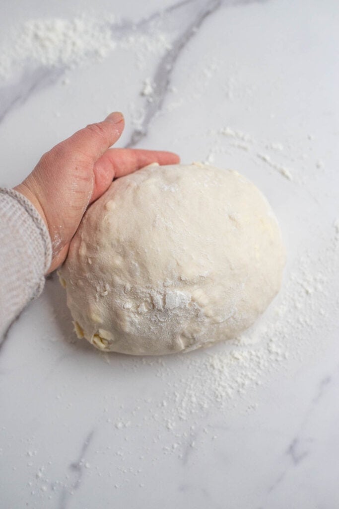 A ball of dough turned out on the counter with flour to shape.