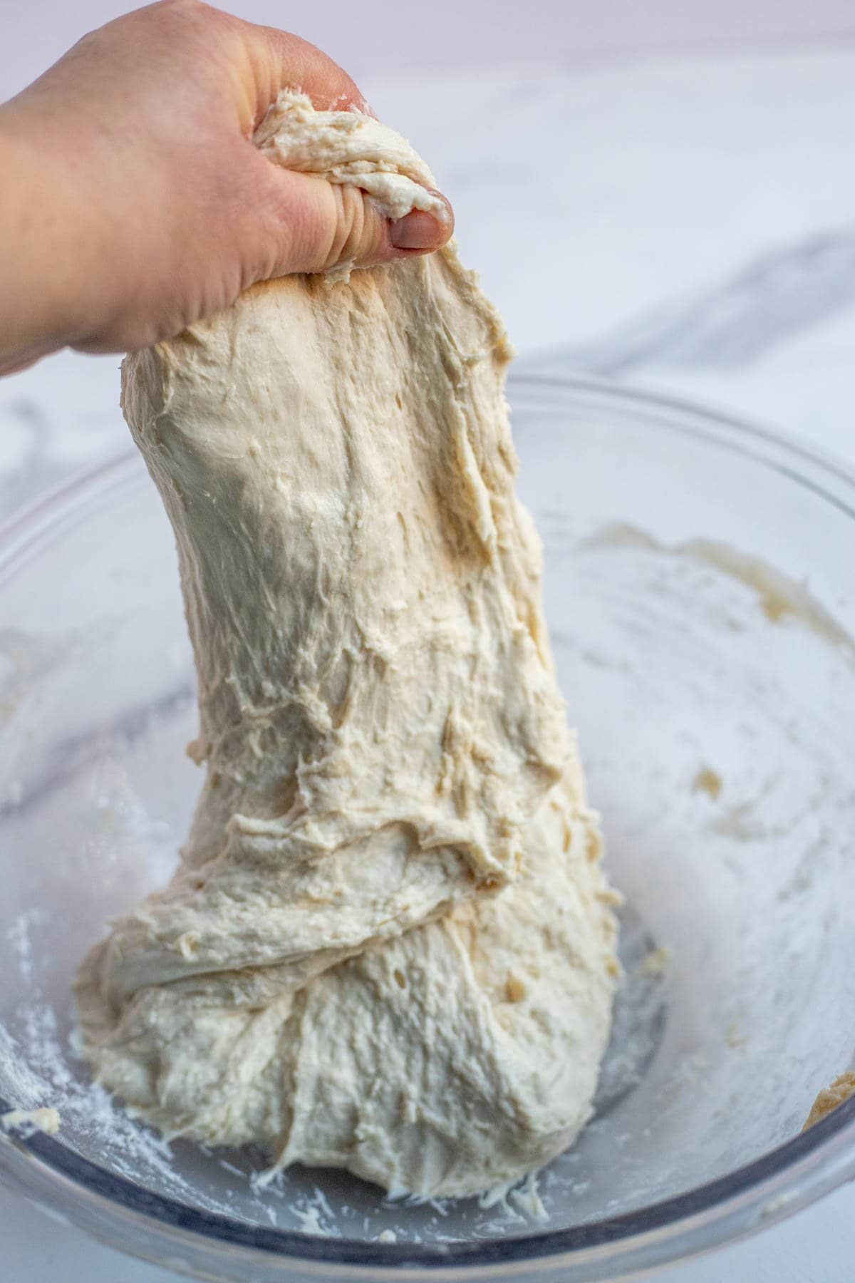 A hand reaching into the bowl and grabbing the dough and stretching it upwards.