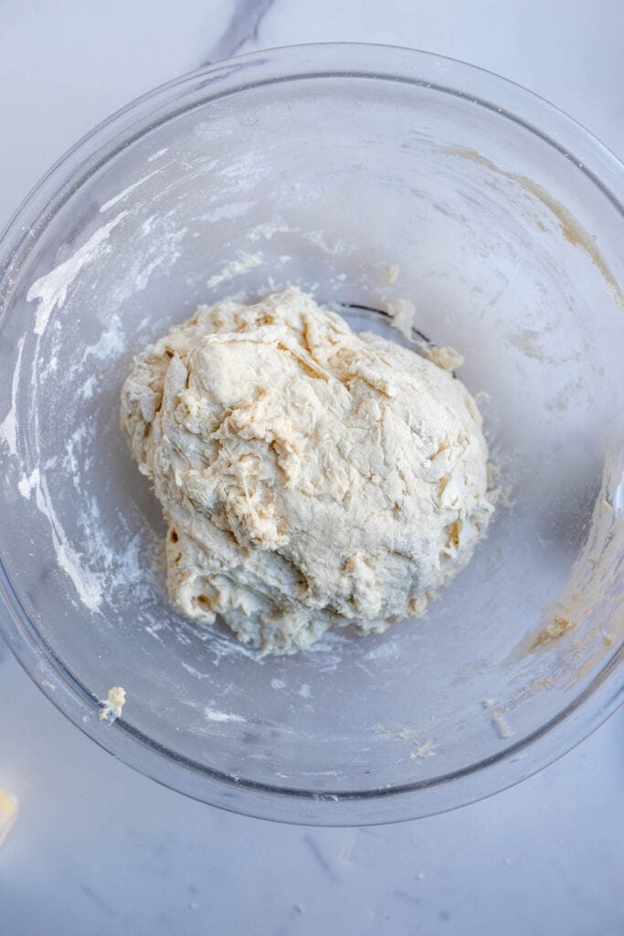 Shaggy bread dough in a glass bowl on the counter.