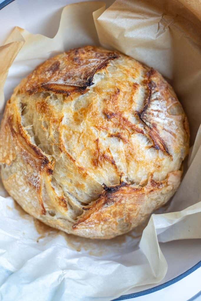 A crusty loaf of sourdough croissant bread on a piece of parchment paper.