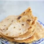 10 freshly made tortillas sitting on a blue plate.