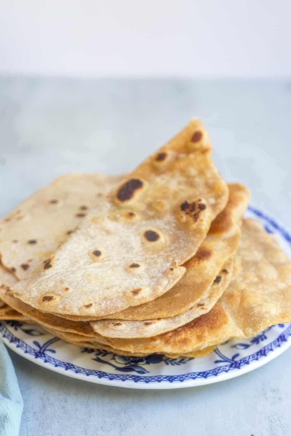 10 freshly made tortillas sitting on a blue plate.