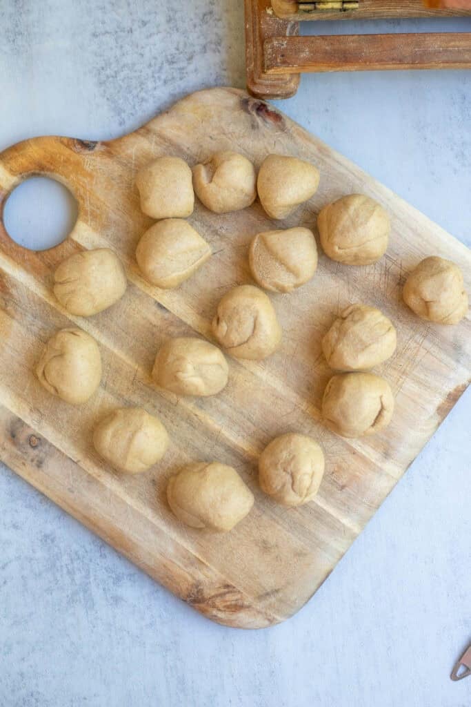 16 dough balls placed on a square wooden cutting board.