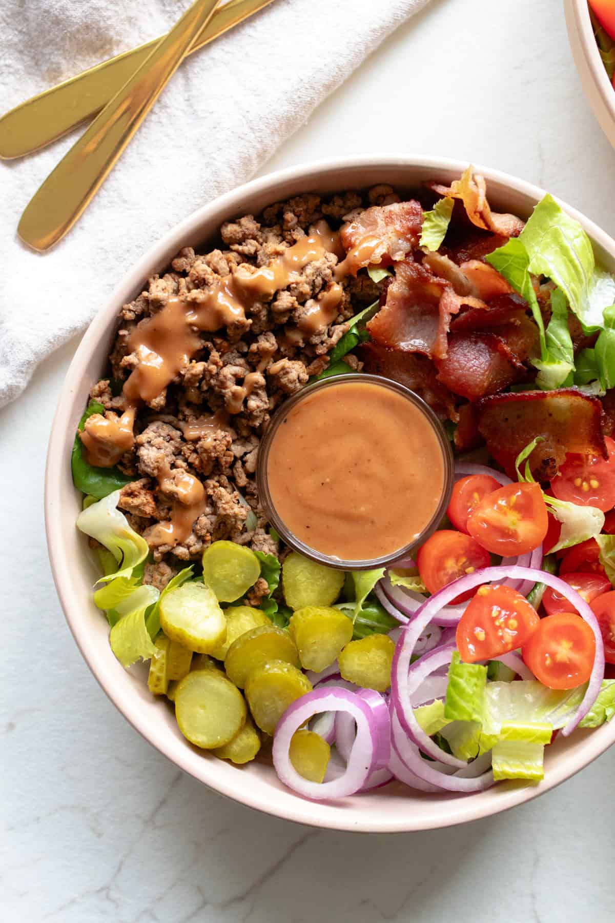 A bowl full of burger fixings, including a smaller bowl of special sauce. 
