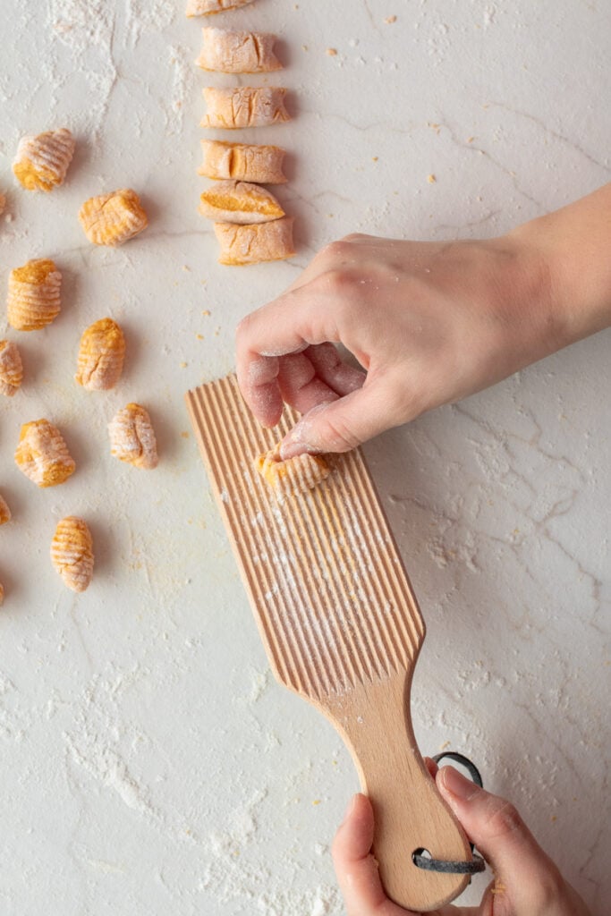 Shaping gnocchi on a wooden grooved board.