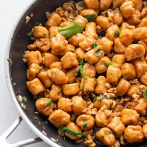A skillet full of pumpkin gnocchi tossed in a sage butter sauce and topped with fresh sage.