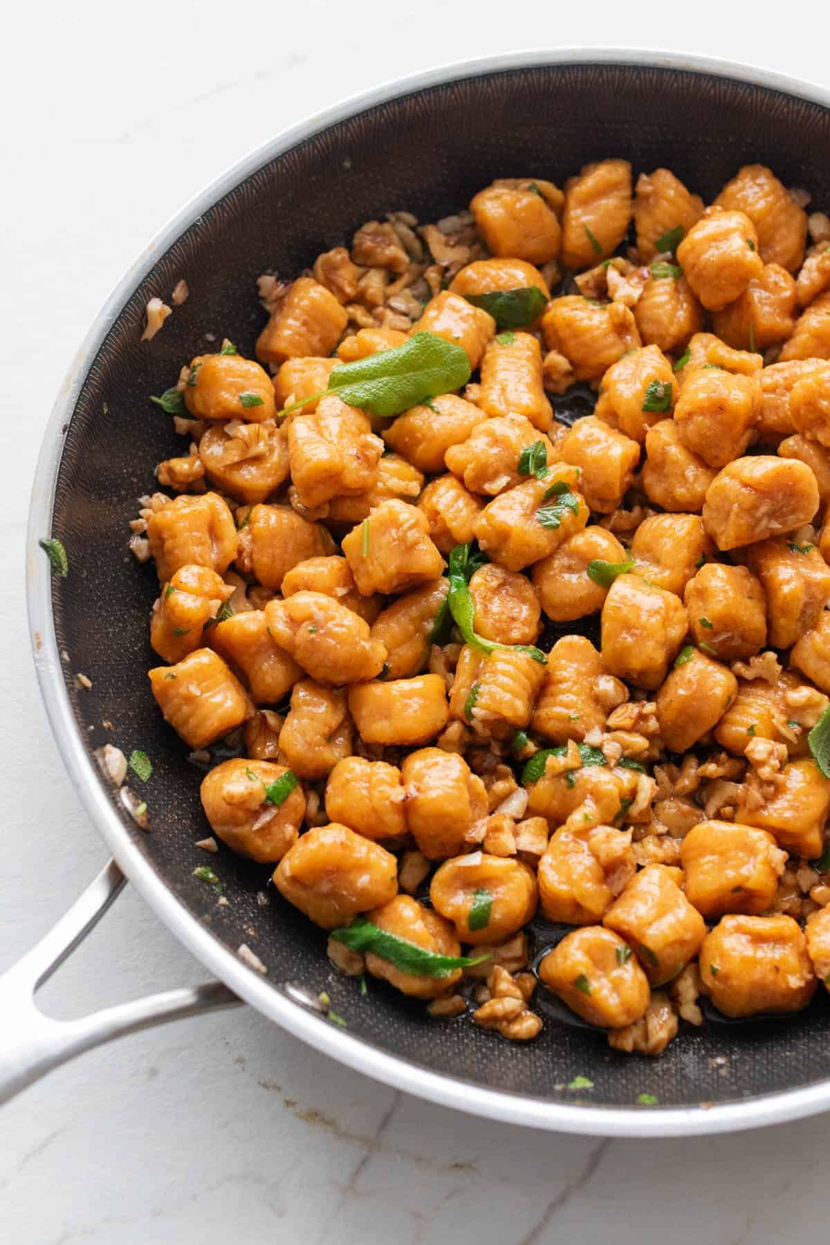 A skillet full of pumpkin gnocchi tossed in a sage butter sauce and topped with fresh sage.