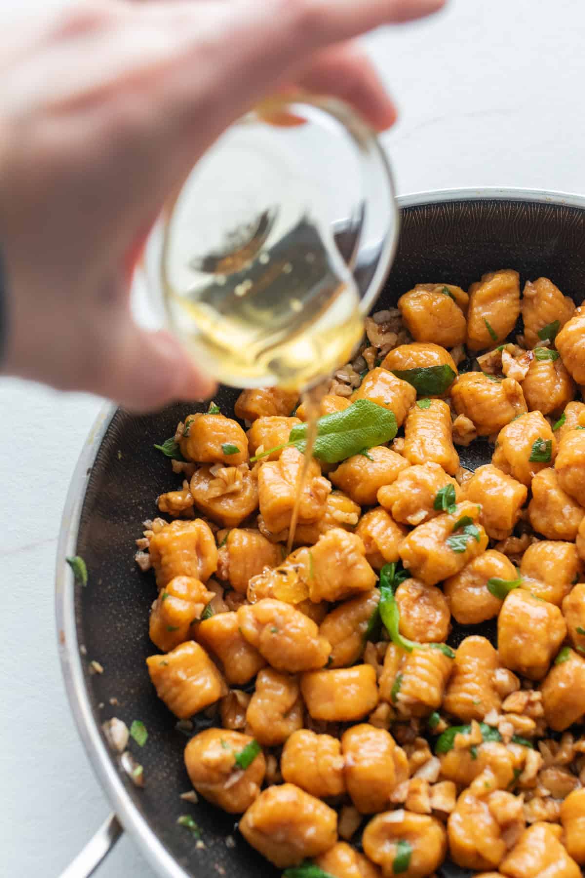 Drizzling honey over pumpkin gnocchi with sage butter sauce in a skillet.