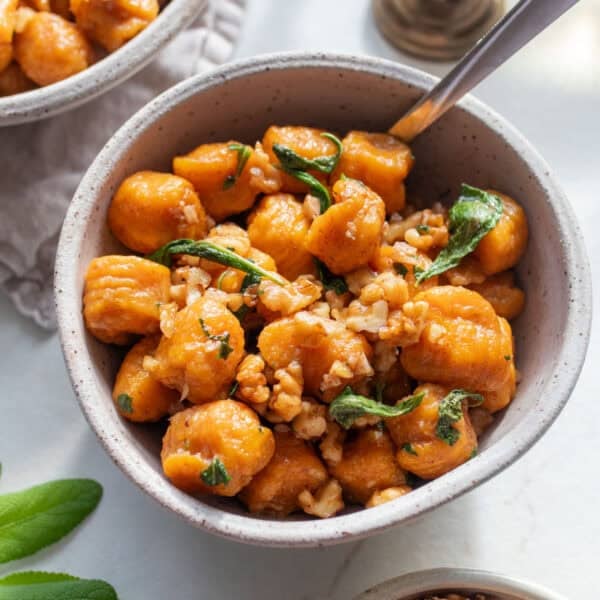 Pumpkin gnocchi with sage butter sauce topped with fresh sage in a white bowls on a countertop.