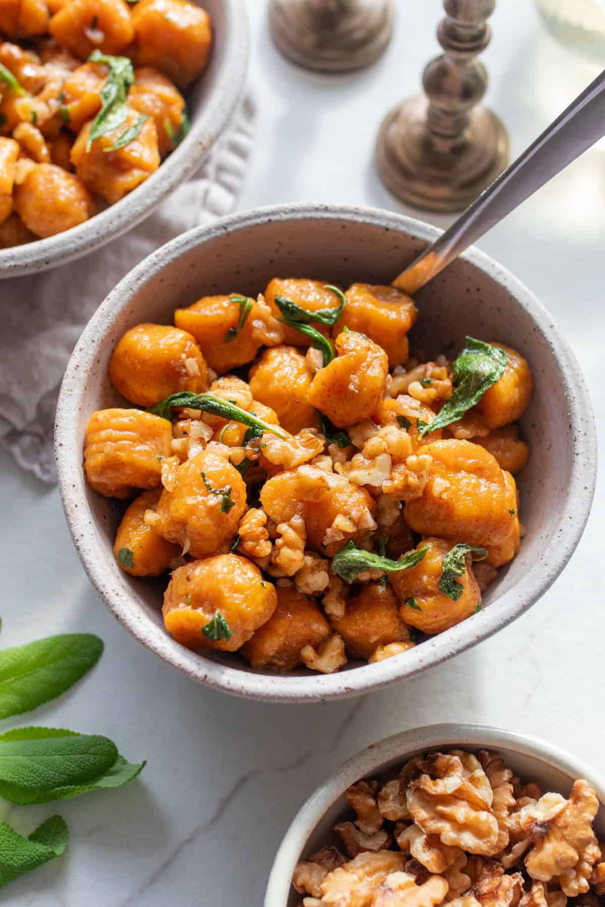 Pumpkin gnocchi with sage butter sauce topped with fresh sage in a white bowl on a countertop.