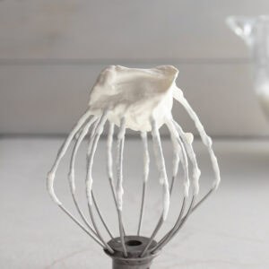 Whipped cream on a balloon whisk standing on a countertop.
