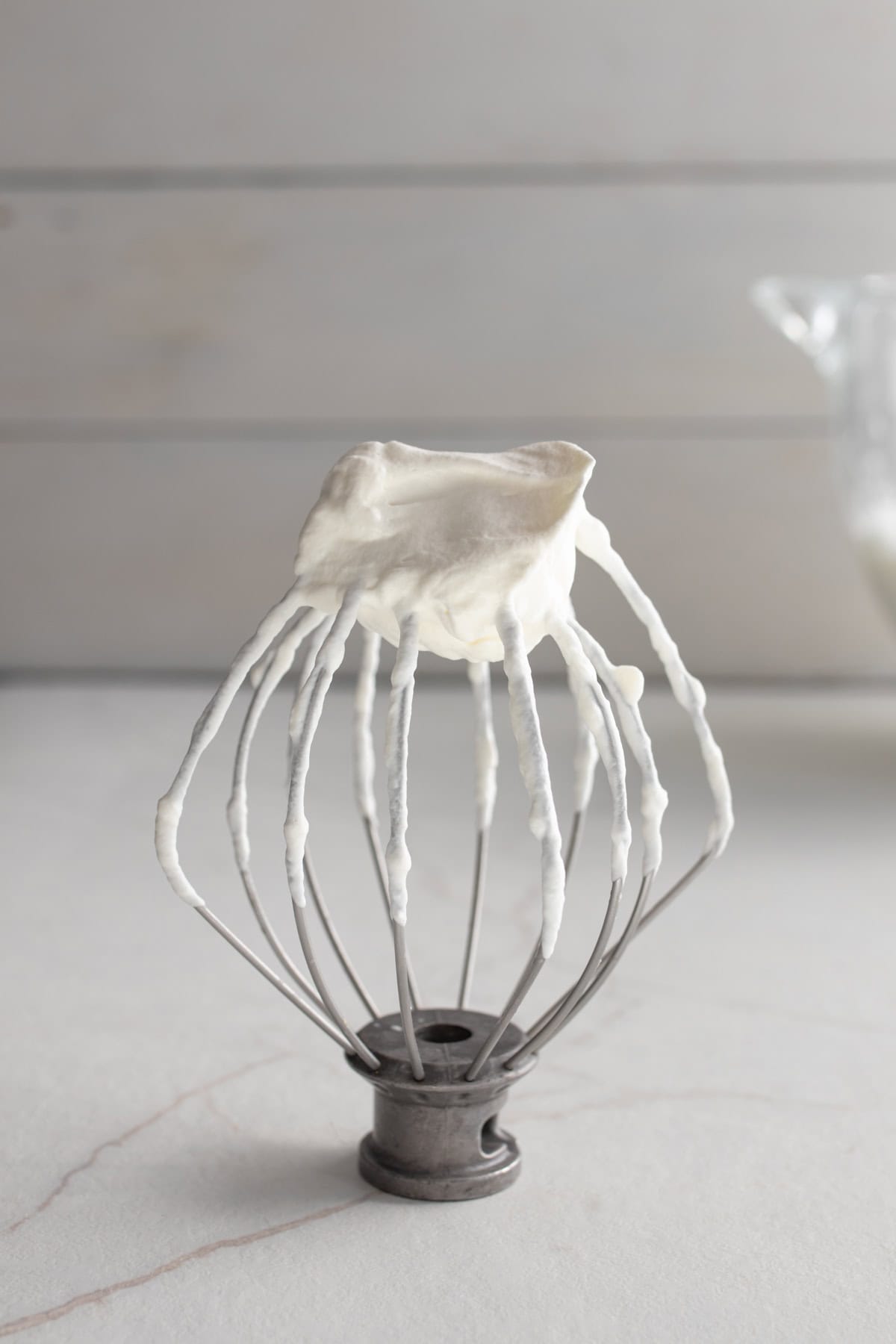 Whipped cream on a balloon whisk standing on a countertop.