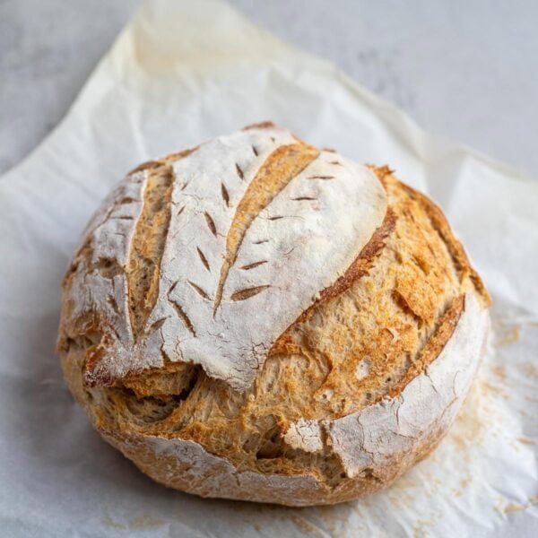 A sourdough boule that has been scored and baked on a piece of parchment paper.