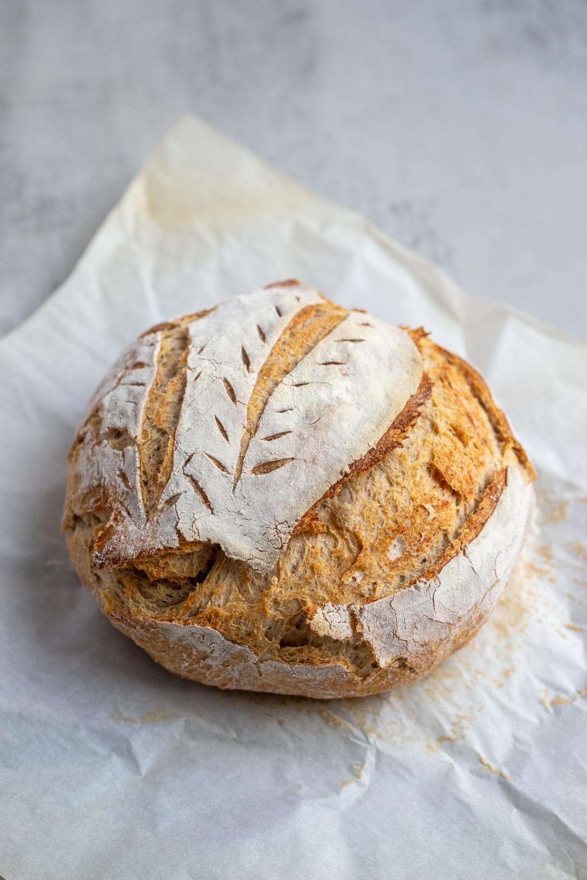 A sourdough boule that has been scored and baked on a piece of parchment paper.