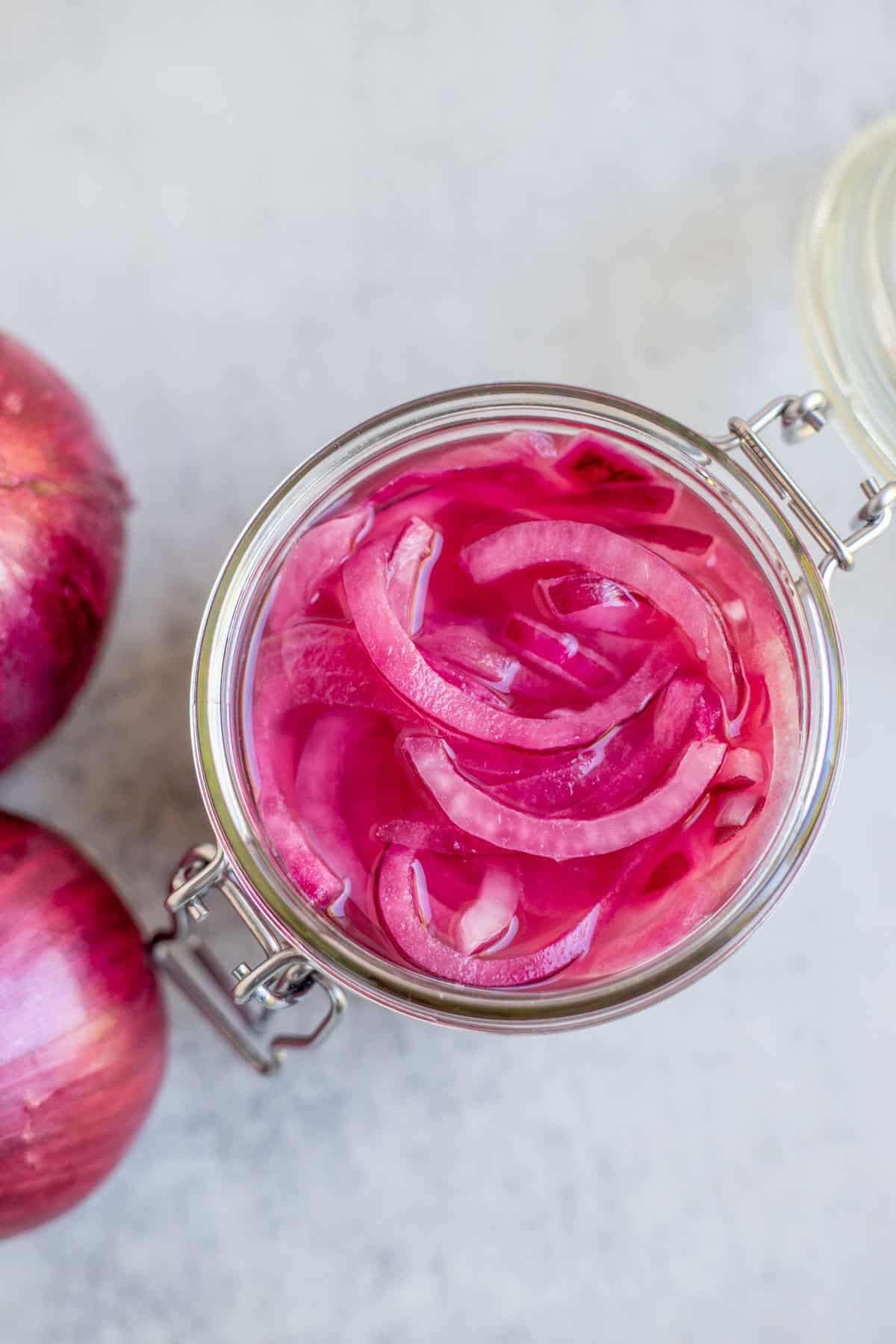 A glass pint jar full of fermented red onions with two whole onions beside the jar.