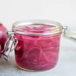 a glass jar of fermented red onions on the counter.