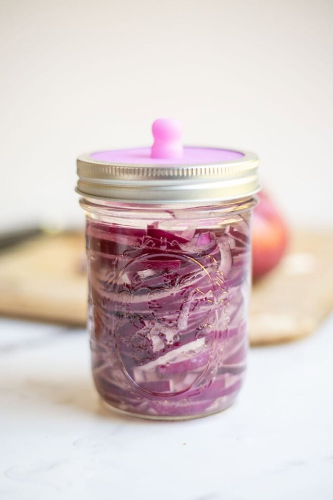 Onions in a glass jar with a fermentation lid fermenting on the counter.