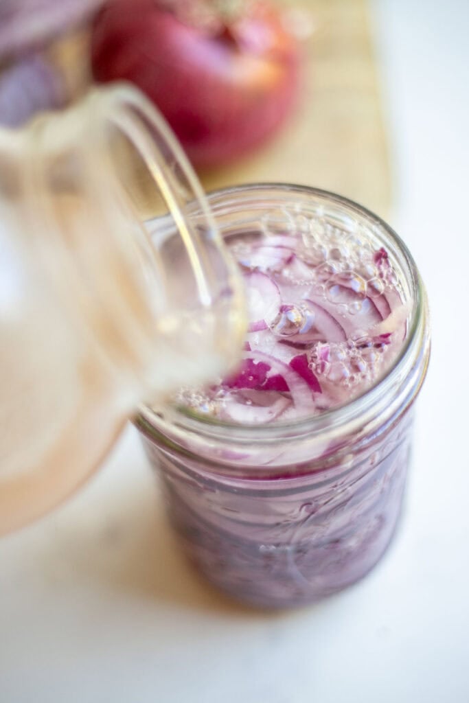 Pouring salt water brine over diced red onions in a jar.