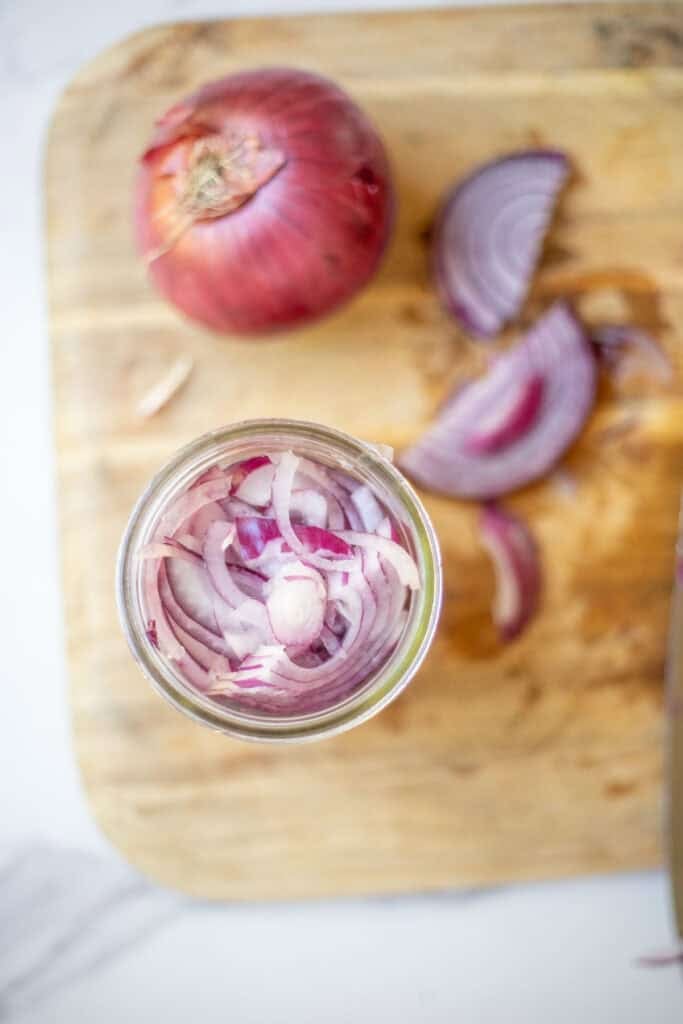 Sliced red onions packed into a jar sitting on a cutting board.