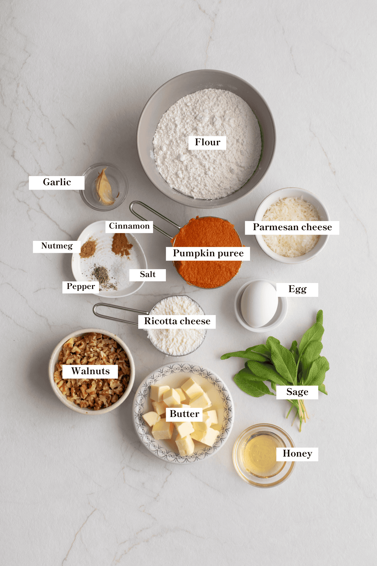 Flour, eggs, sage, pumpkin puree, and other ingredients for pumpkin gnocchi spread out on a countertop.