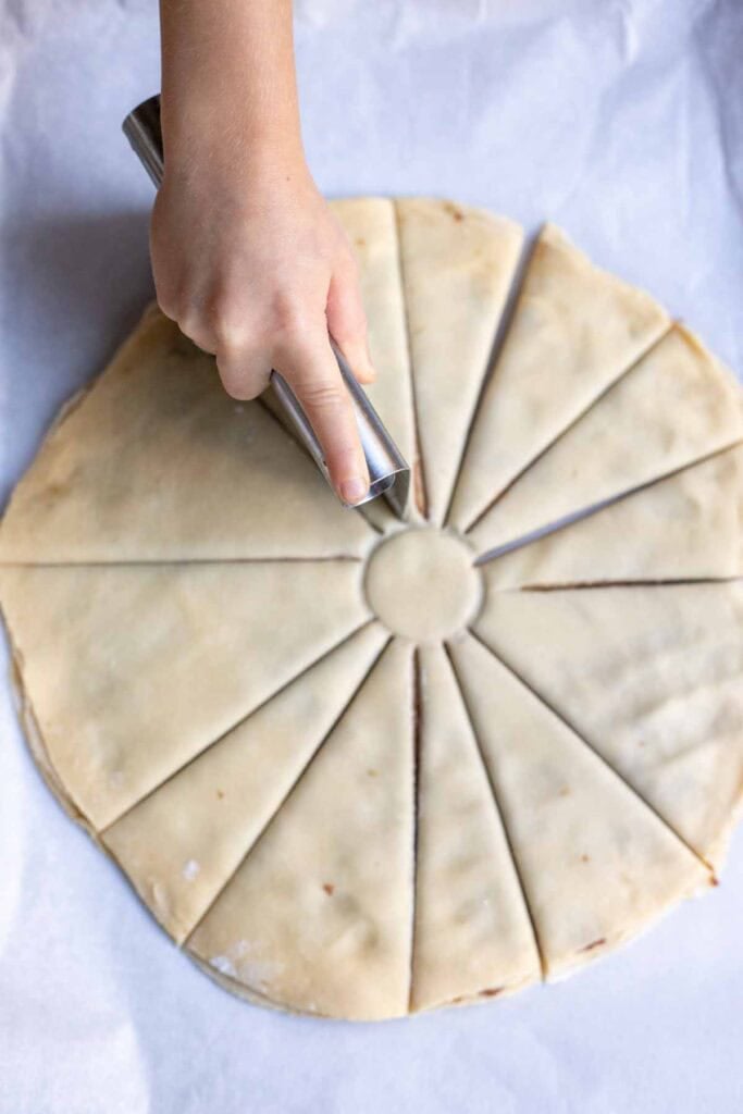 A hand cutting 12 lines in the rounds of dough, but leaving the middle circle intact.