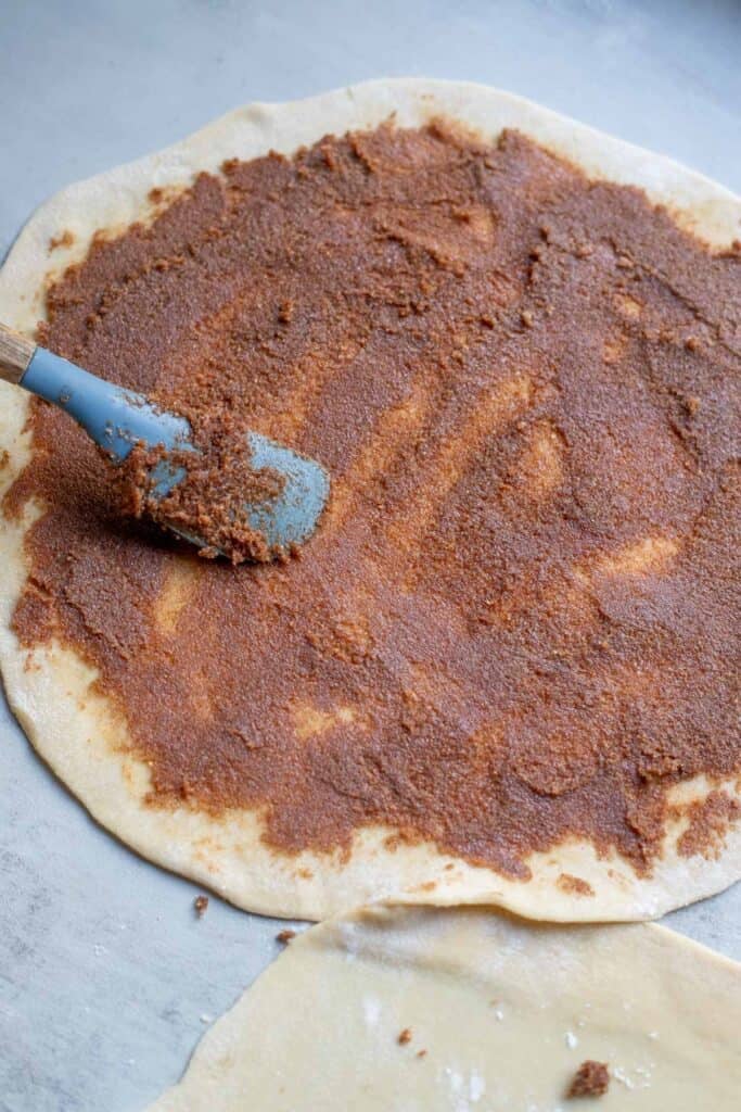 A spatula spreading the cinnamon, sugar, and butter mixture over the rolled out dough.