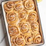 twelve sourdough orange cinnamon rolls baked in a dish and drizzled with an orange glaze.