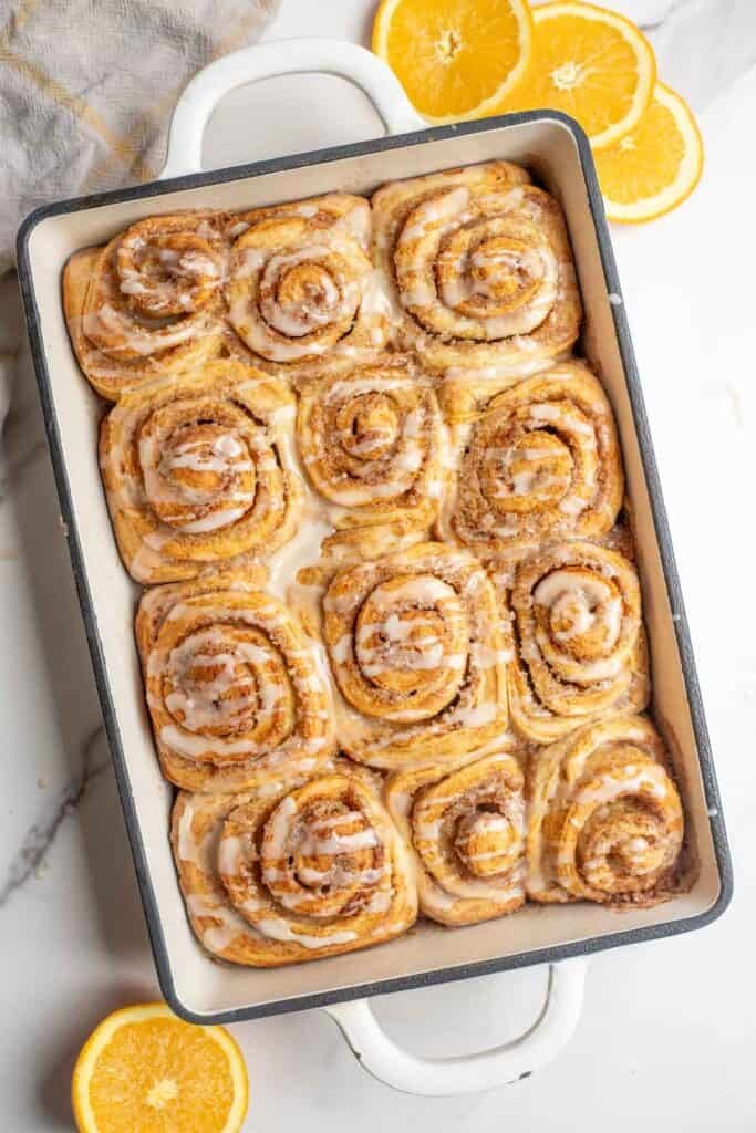 Twelve sourdough orange cinnamon rolls baked in a dish and drizzled with an orange glaze.