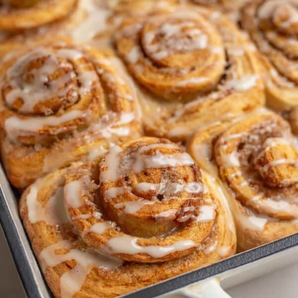 a baking dish of freshly baked sourdough orange cinnamon rolls with a citrus glaze.