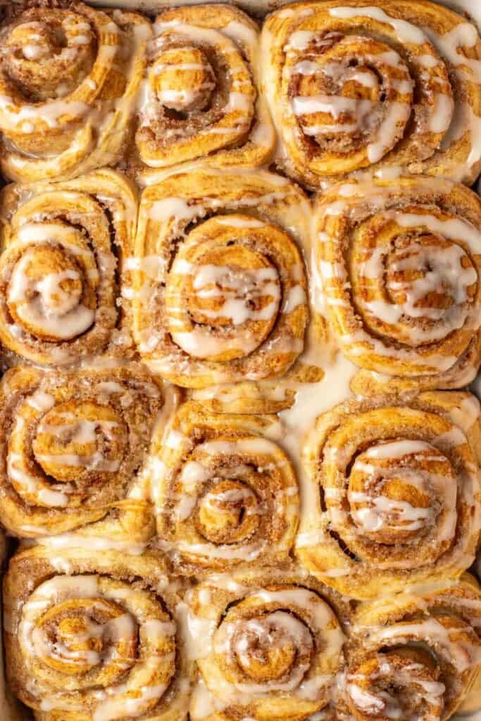 fresh baked orange cinnamon rolls in a pan drizzled with an orange glaze.