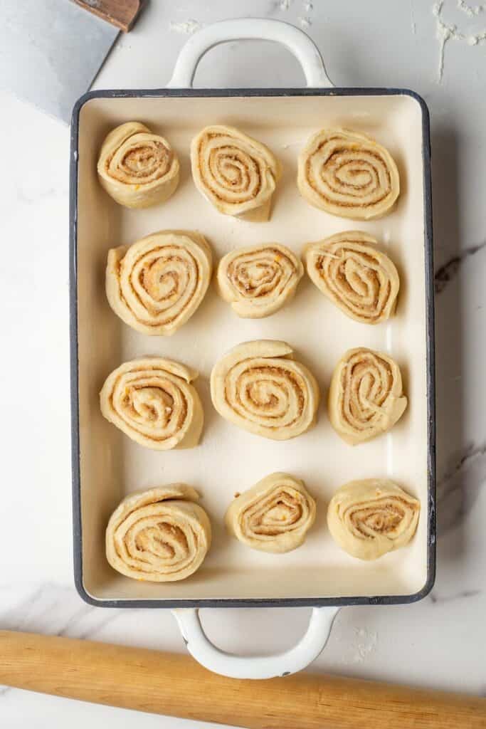 Twelve unbaked orange cinnamon rolls in a baking dish. 