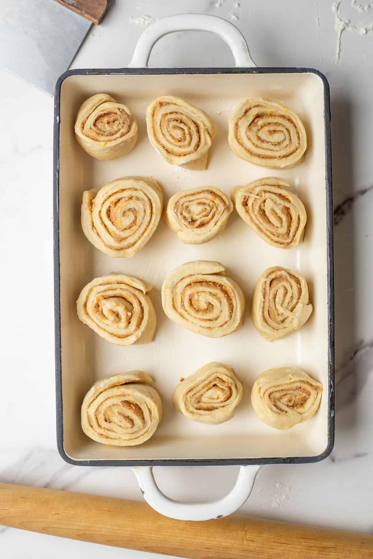 Twelve unbaked orange cinnamon rolls in a baking dish.