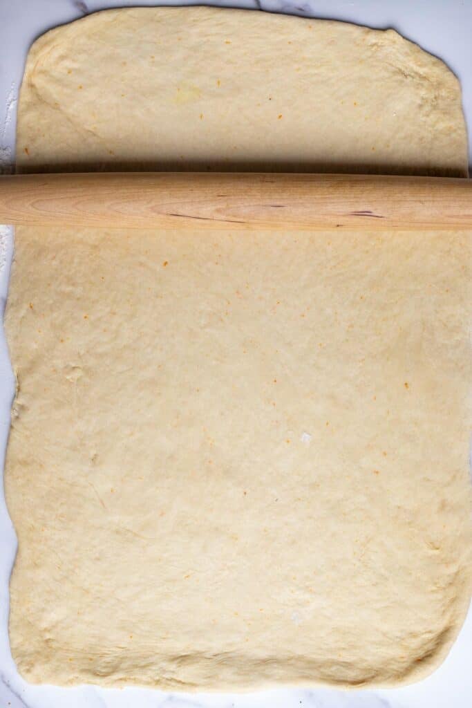 Sourdough cinnamon roll dough rolled out on a counter with a rolling pin.