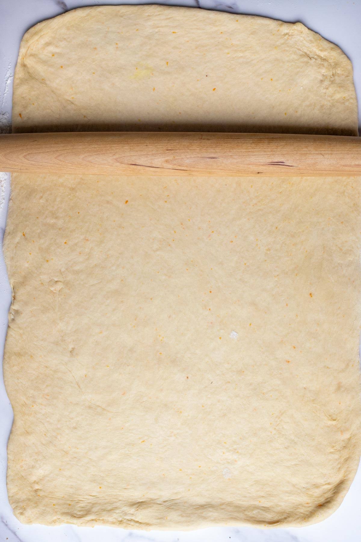 Sourdough cinnamon roll dough rolled out on a counter with a rolling pin.
