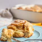 an orange cinnamon roll made with sourdough on a blue plate with one bite on the end of a fork.
