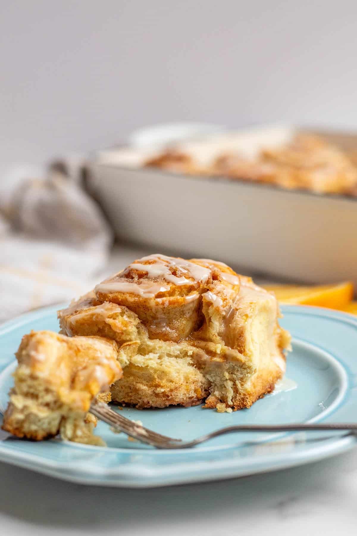 An orange cinnamon roll made with sourdough on a blue plate with one bite on the end of a fork.