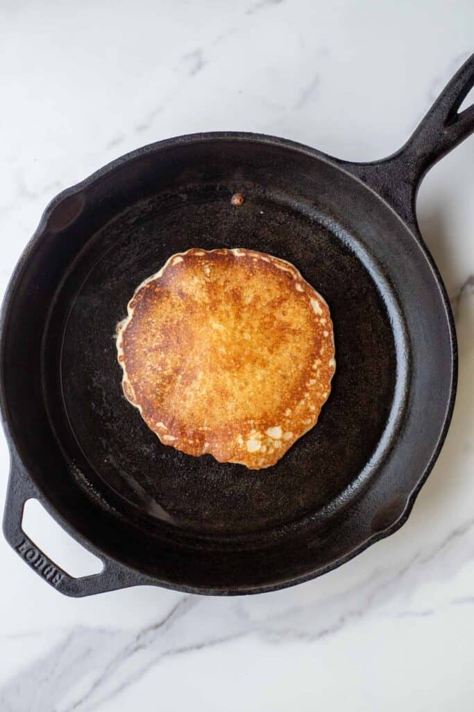 A sourdough pancake lightly browned in a cast iron skillet.