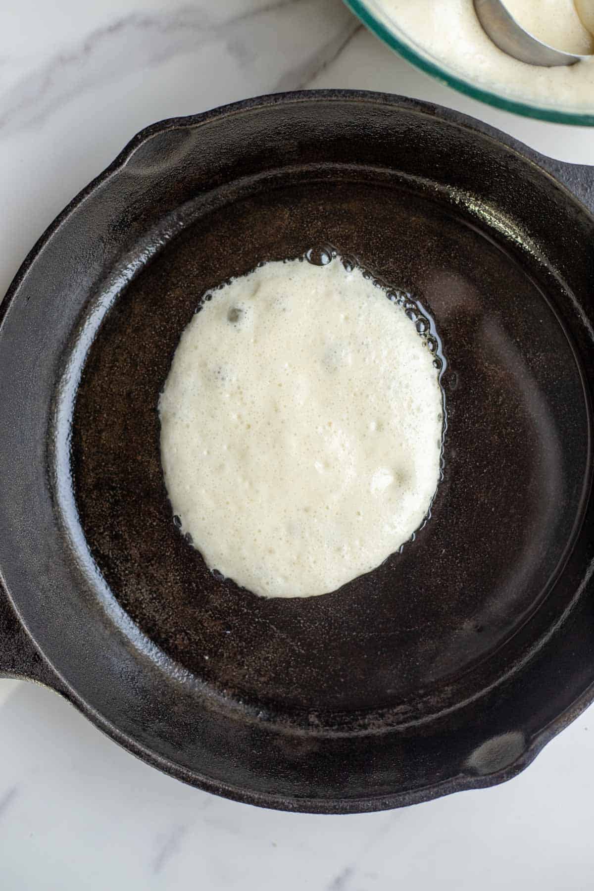 A cast iron skillet with melted butter and pancake batter poured into the skillet.
