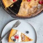 a slice of a dutch baby pancake from the cast iron skillet on a white serving plate.