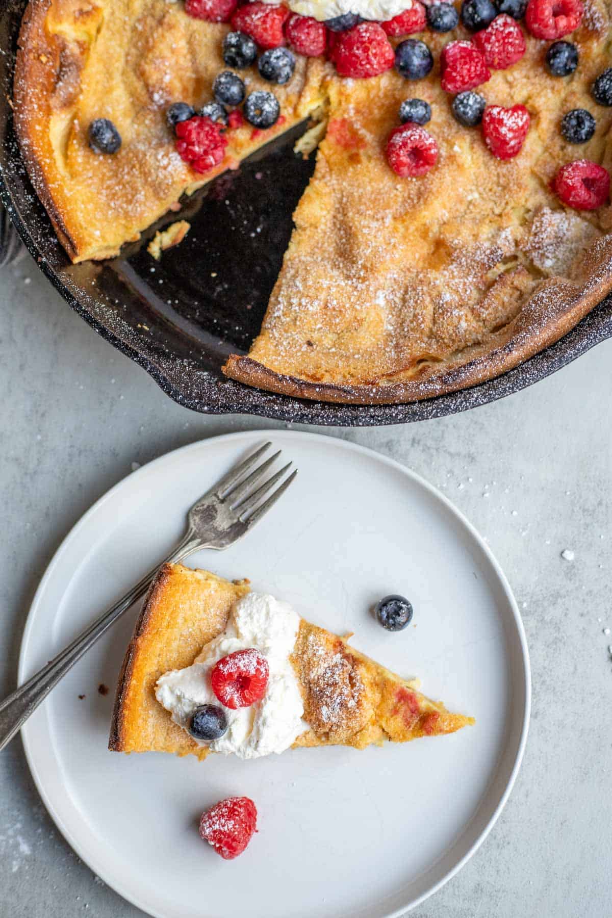 A slice of a Dutch baby pancake from the cast iron skillet on a white serving plate.