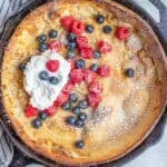 a cast iron skillet with a dutch baby pancake topped with fresh berries and whipped cream.